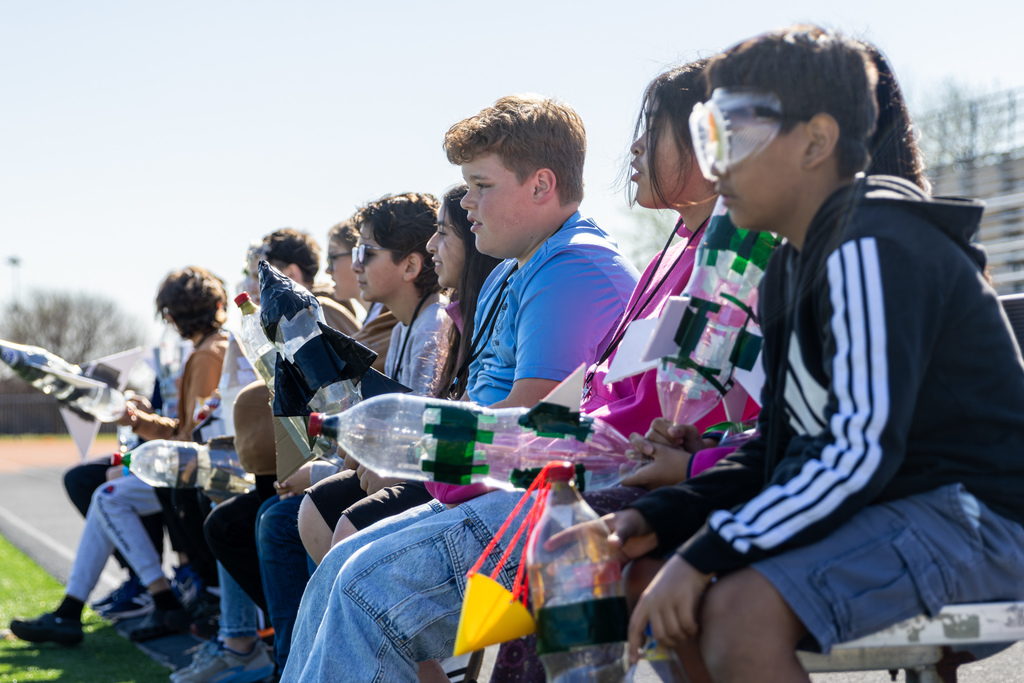 students holding their bottle rockets while seated on a bench
