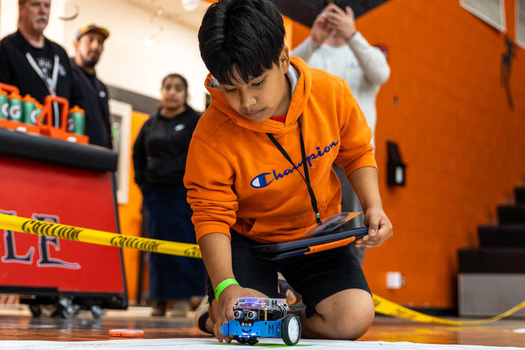 a student adjusting their robot on a gym floor