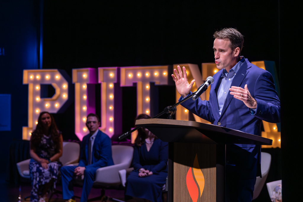 Man speaking a podium with finalists looking on from behind