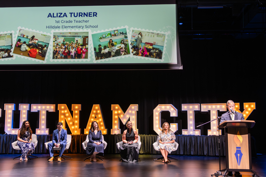 Teacher of the Year finalists on stage with a man presenting at the podium