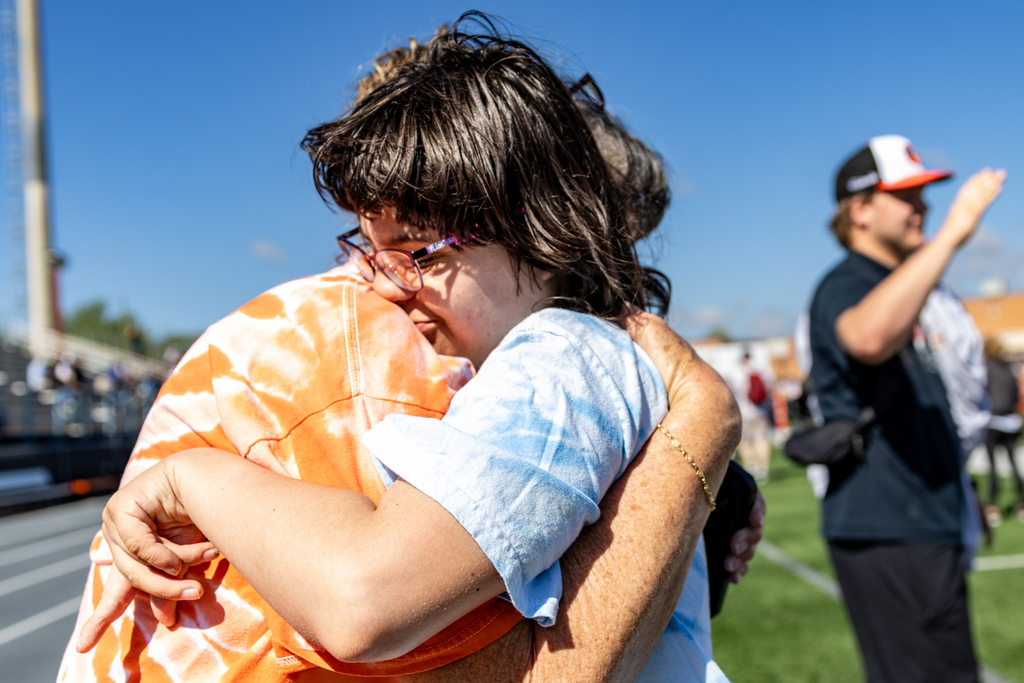 A student hugs an adult on the field, holding on tightly while others stand nearby in the background.