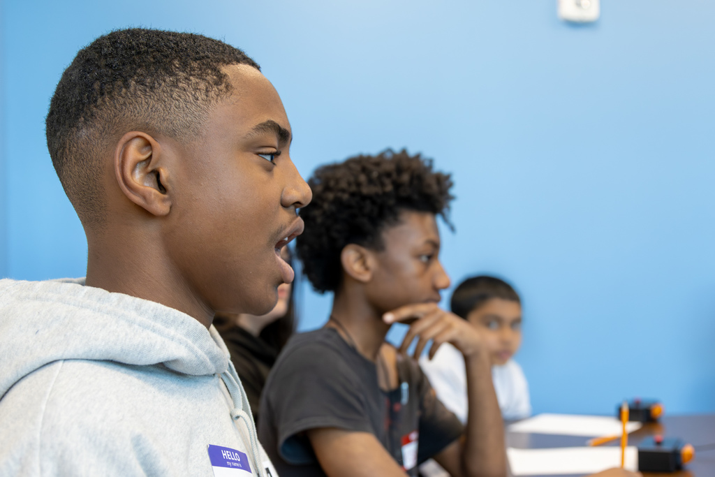 A student answers a question during a quiz bowl round while teammates sit beside him, listening and thinking.