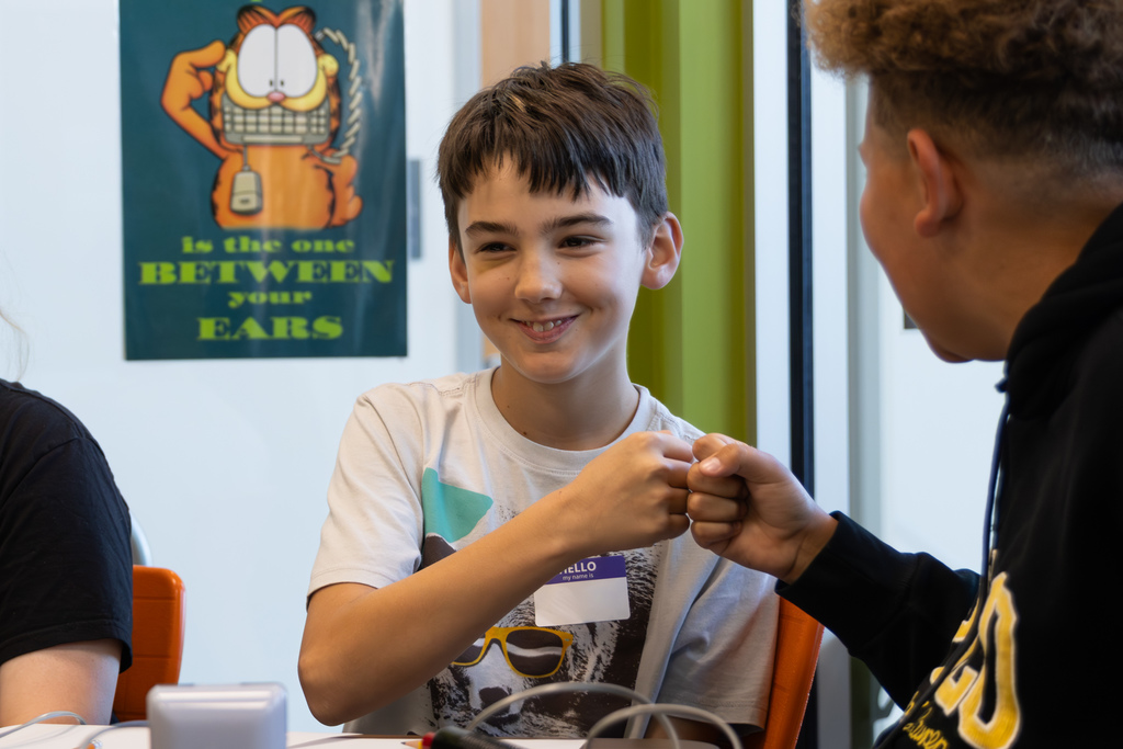 Two students share a quick fist bump at the table after a successful moment during a quiz bowl match.
