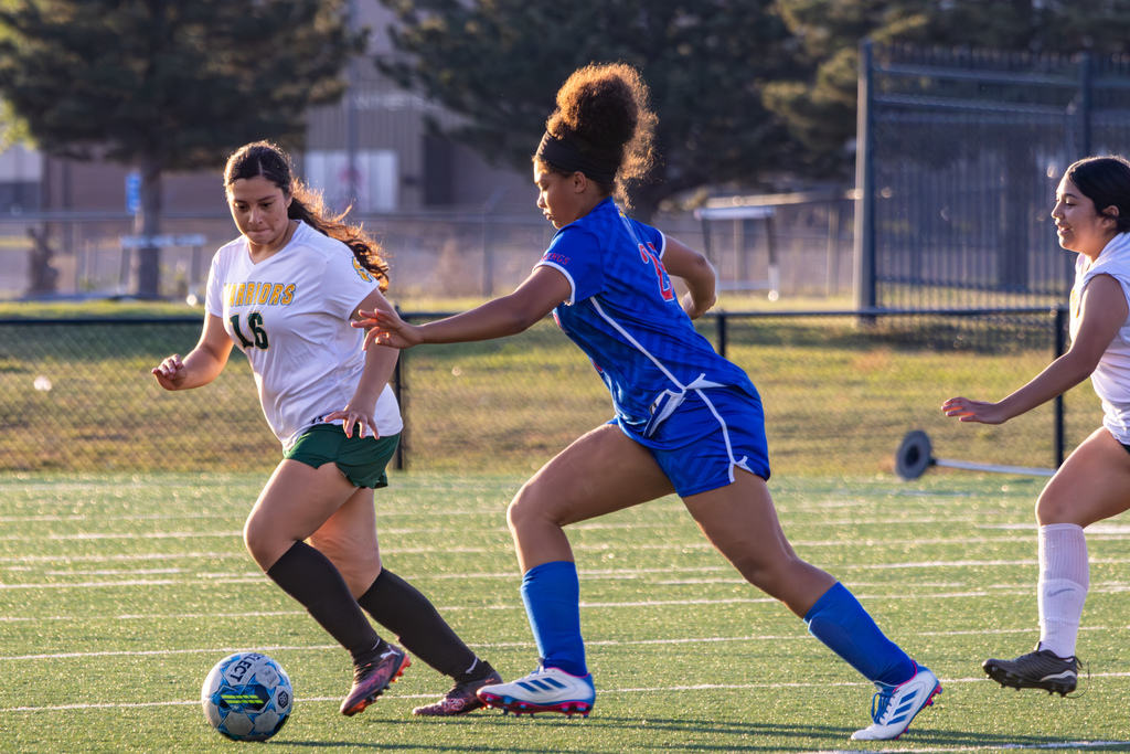 A Warriors player in white dribbles forward while a Hefner defender in blue steps in to challenge, both mid-stride on the field.