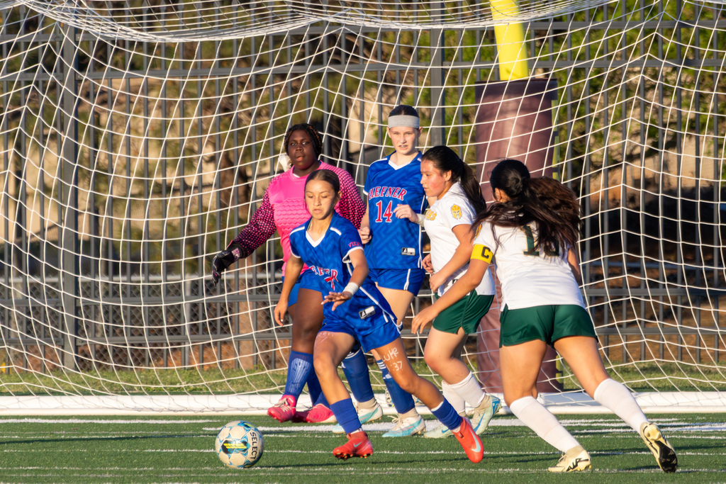 Multiple players gather in front of the goal as the ball rolls into the box, with both teams preparing for a shot or clearance.