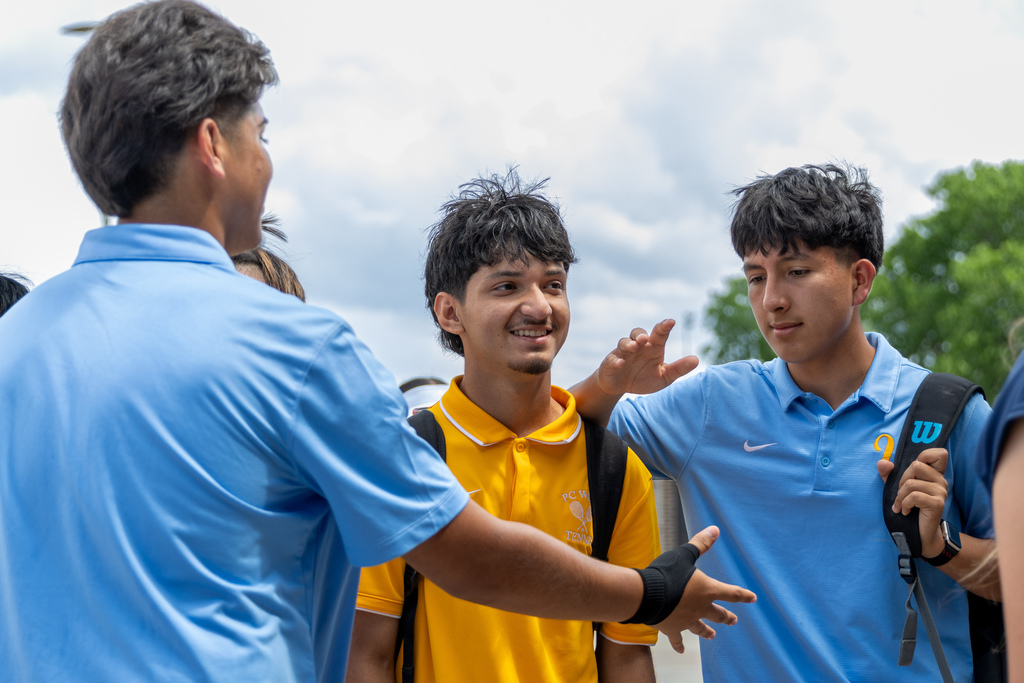 Putnam City West tennis players talk and gesture between matches, smiling and interacting near the courts.