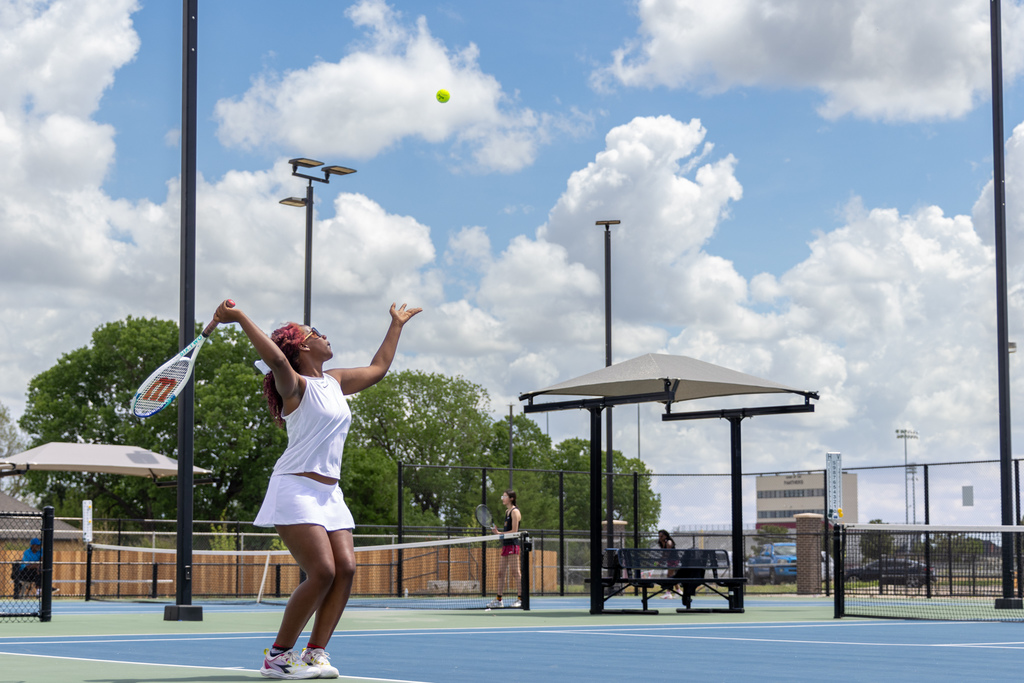 A Putnam City High girls tennis player tosses the ball overhead to begin her serve on an outdoor court.