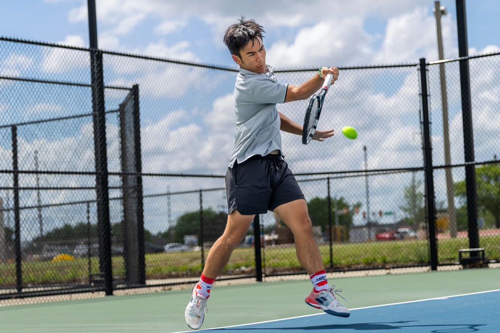 A Putnam City High tennis player swings through a forehand mid-stride, body rotating as the ball approaches his racket.