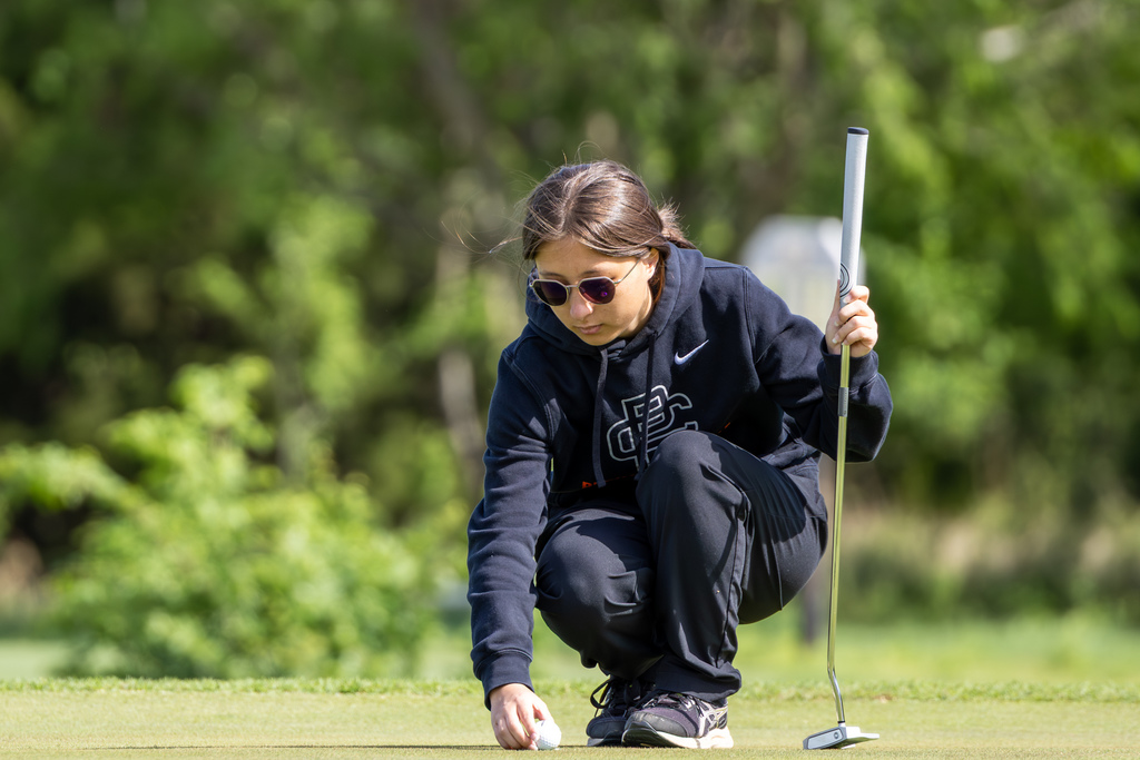 Student golfer crouches to place a ball on the green while holding a putter, preparing for a putt.