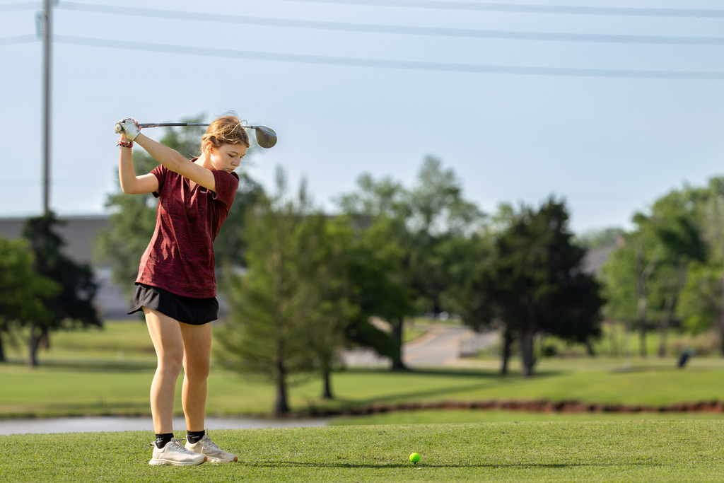 Student golfer at the top of a backswing on a tee box, beginning a drive during competition.