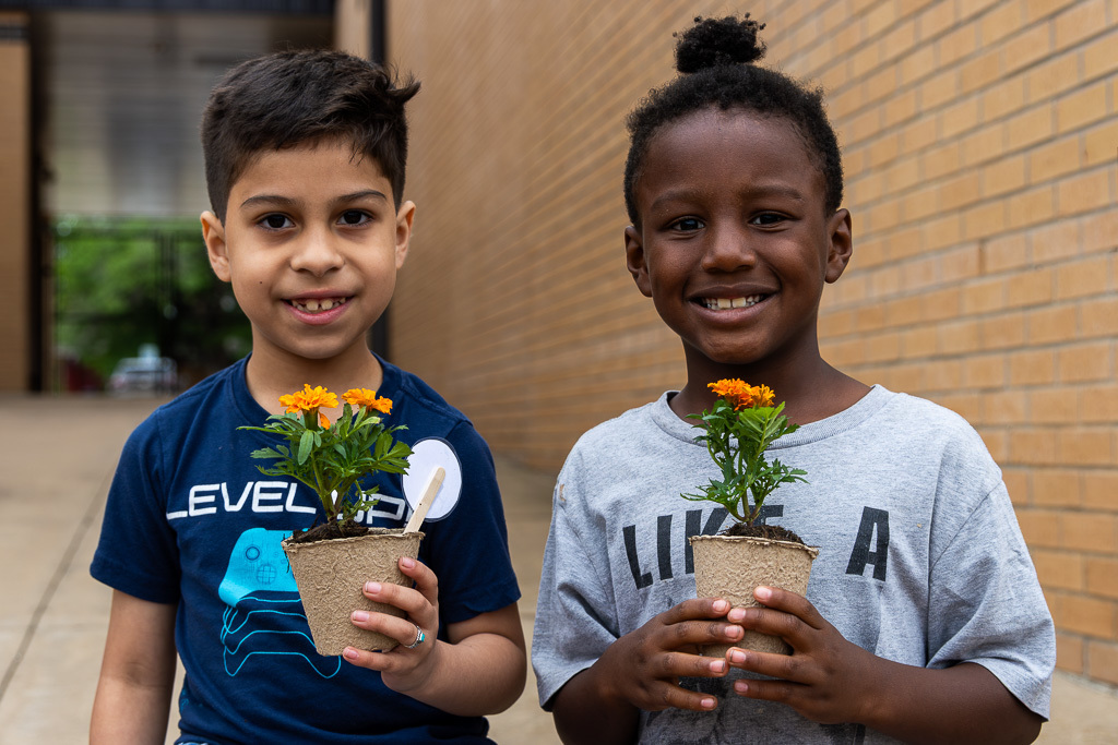 two boys pose with plants they planted