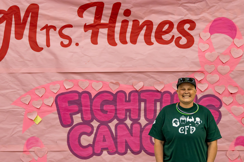 Staff member smiles in front of a large pink “Fight Cancer” display covered in handwritten heart notes.