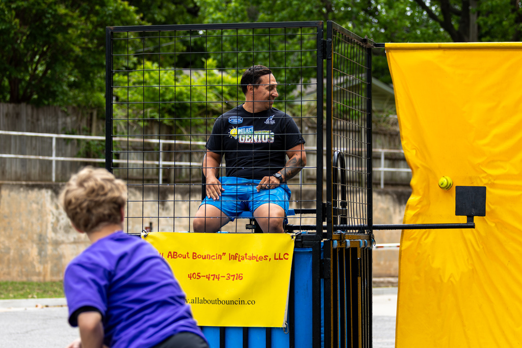 Student throws a ball at a dunk tank, aiming at a staff member seated above the water.