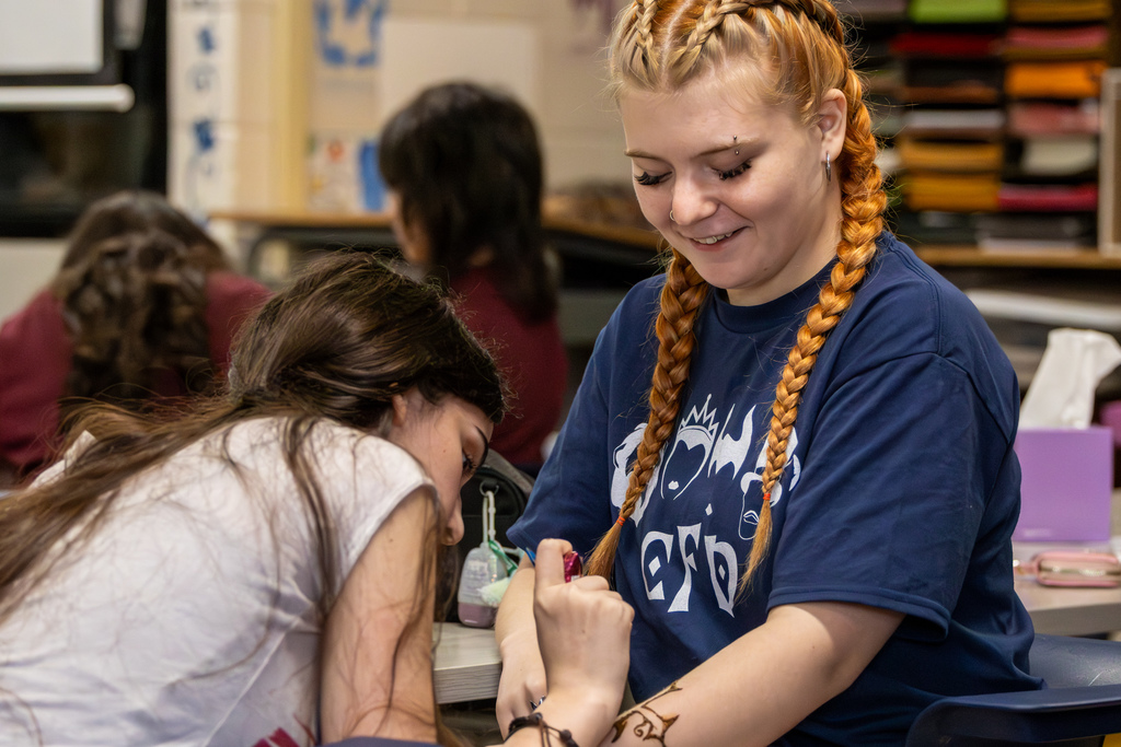Student carefully paints a design on another student’s arm at a table during the event.