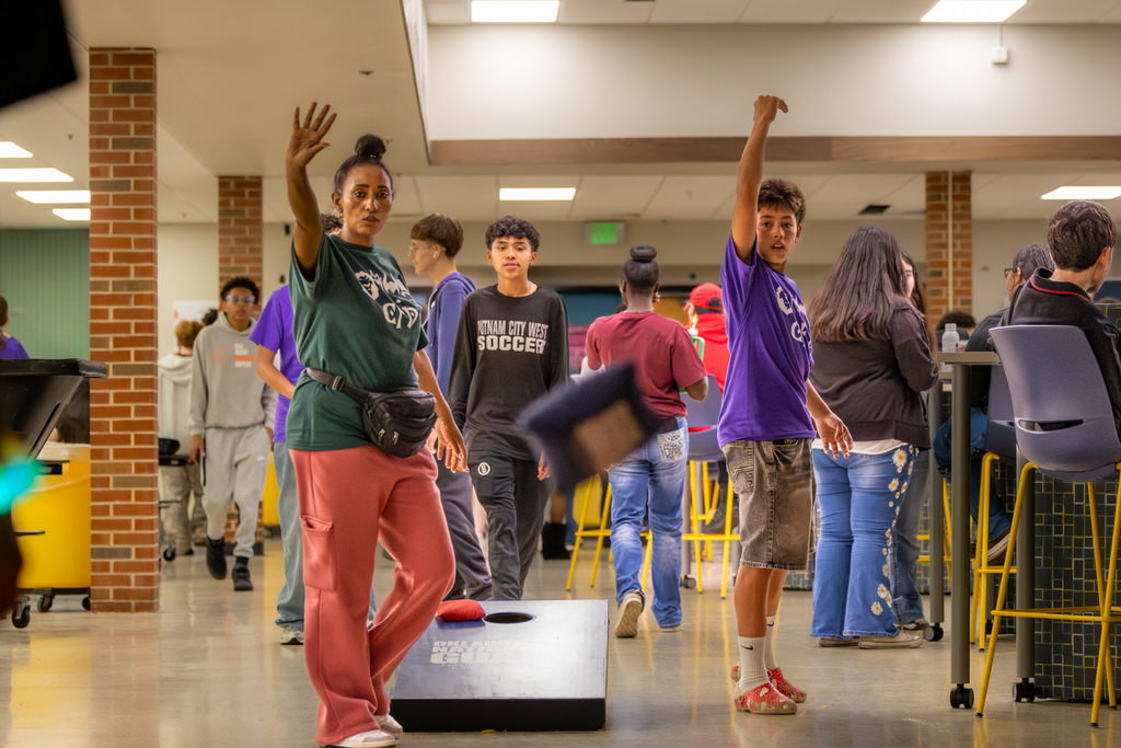 Staff member and students play cornhole in a school common area during CFD Week activities.
