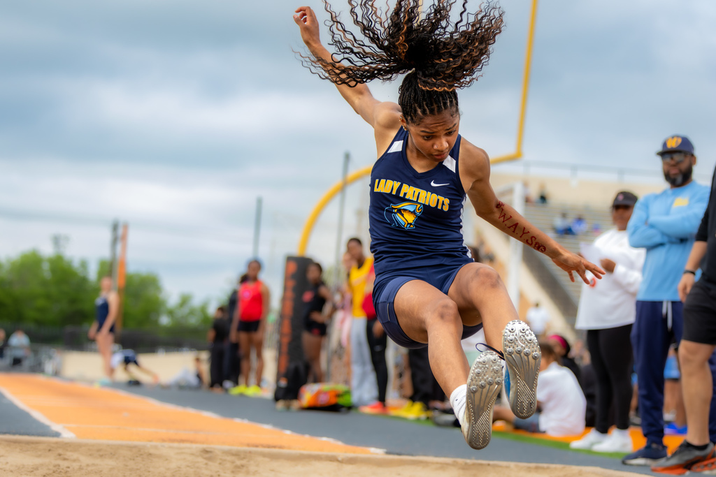Female long jumper from Putnam City West lands in the sand pit, hair flying upward as she completes her jump.