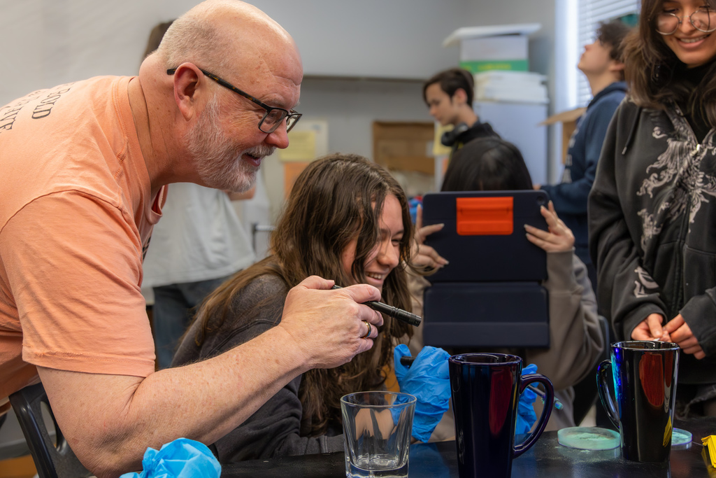 Teacher and student smile while working together at a lab table, using tools to analyze potential evidence.