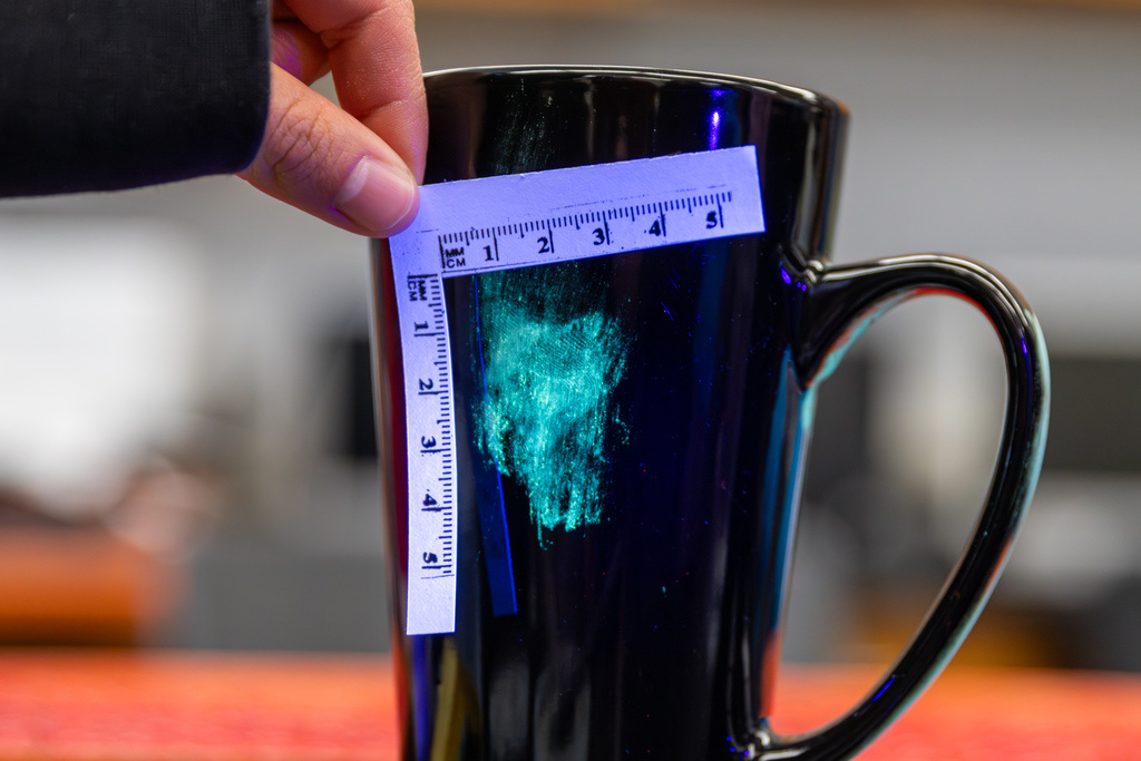 Close-up of a mug with a visible fingerprint, measured with a small ruler for documentation.