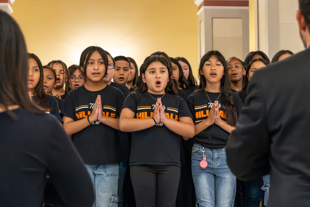 Close-up of students singing with hands together in a choreographed movement during the performance.