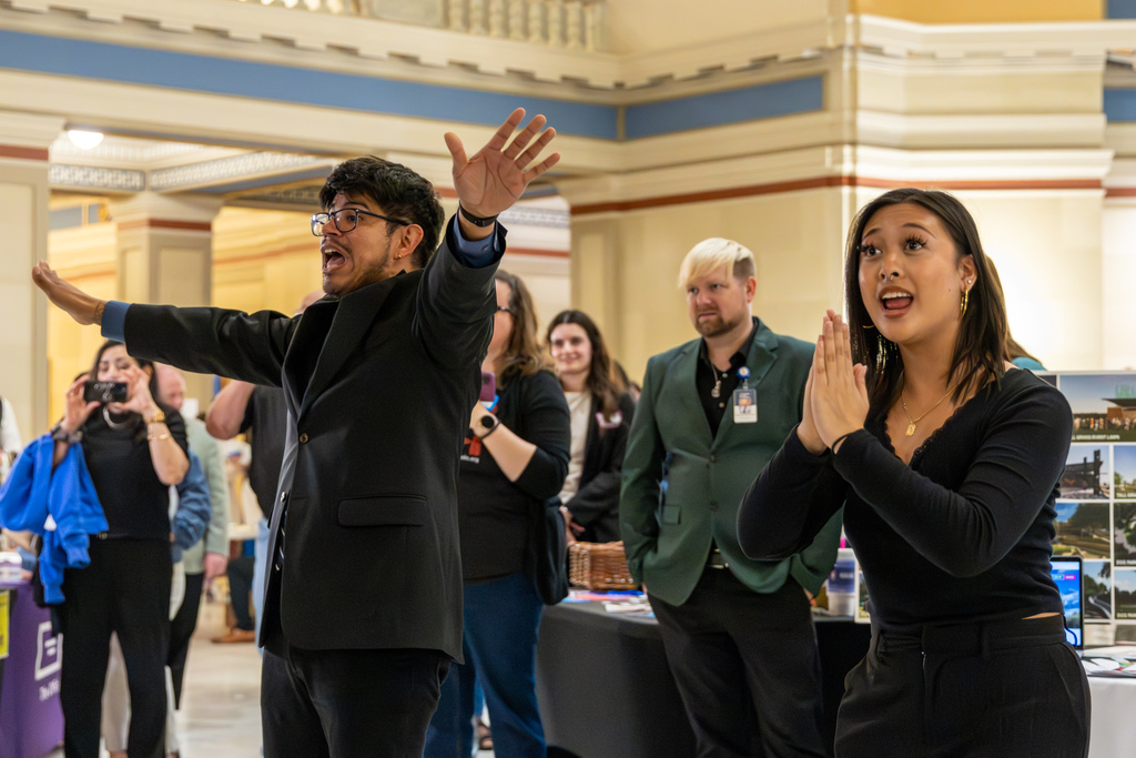 Choir director gestures expressively while leading the performance, with staff and attendees watching nearby.