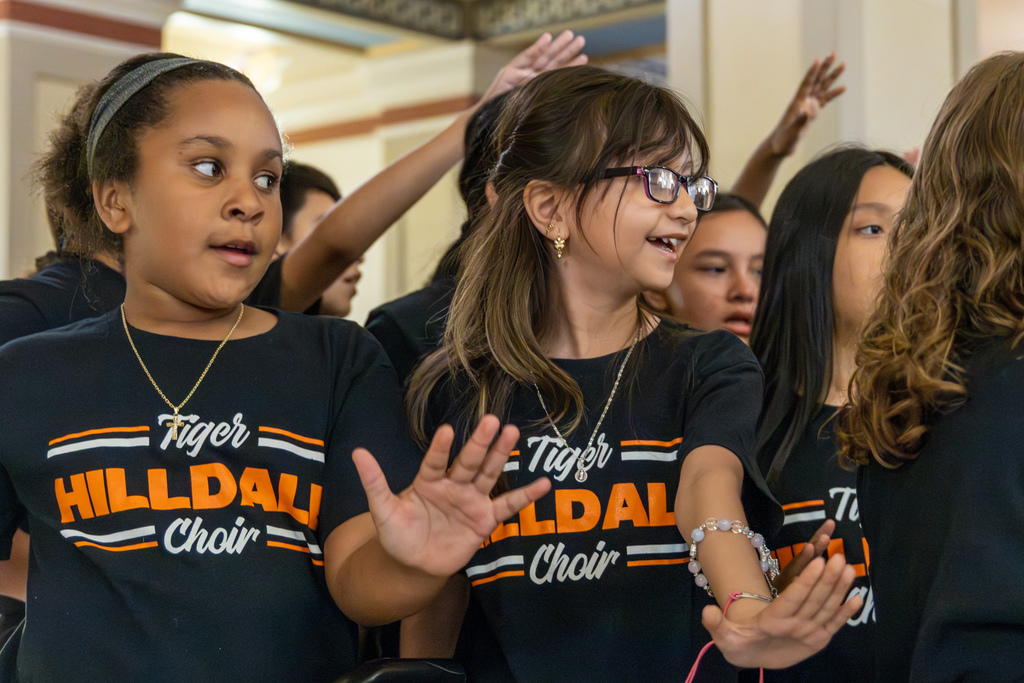 Students perform coordinated hand motions while singing as part of the choir presentation.