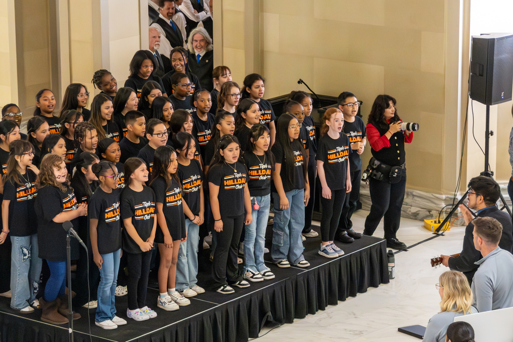 Hilldale Elementary choir performs on a small stage inside the Capitol while a conductor leads.