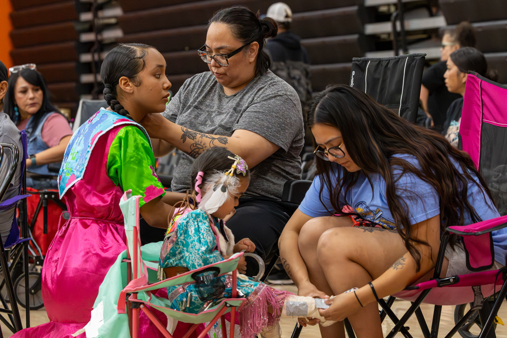 A group helps young dancers adjust clothing and shoes while seated in the gym before or during the Putnam City Youth Powwow.