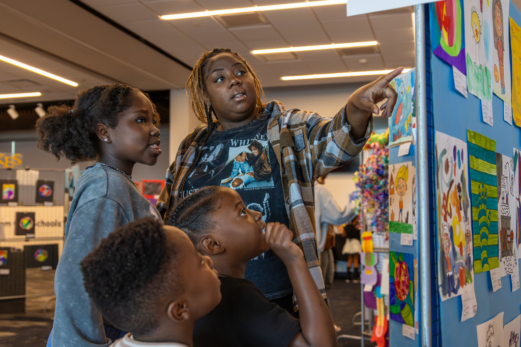 A family looks at student artwork together during the Putnam City Arts Festival, with one adult pointing toward pieces on a display panel.