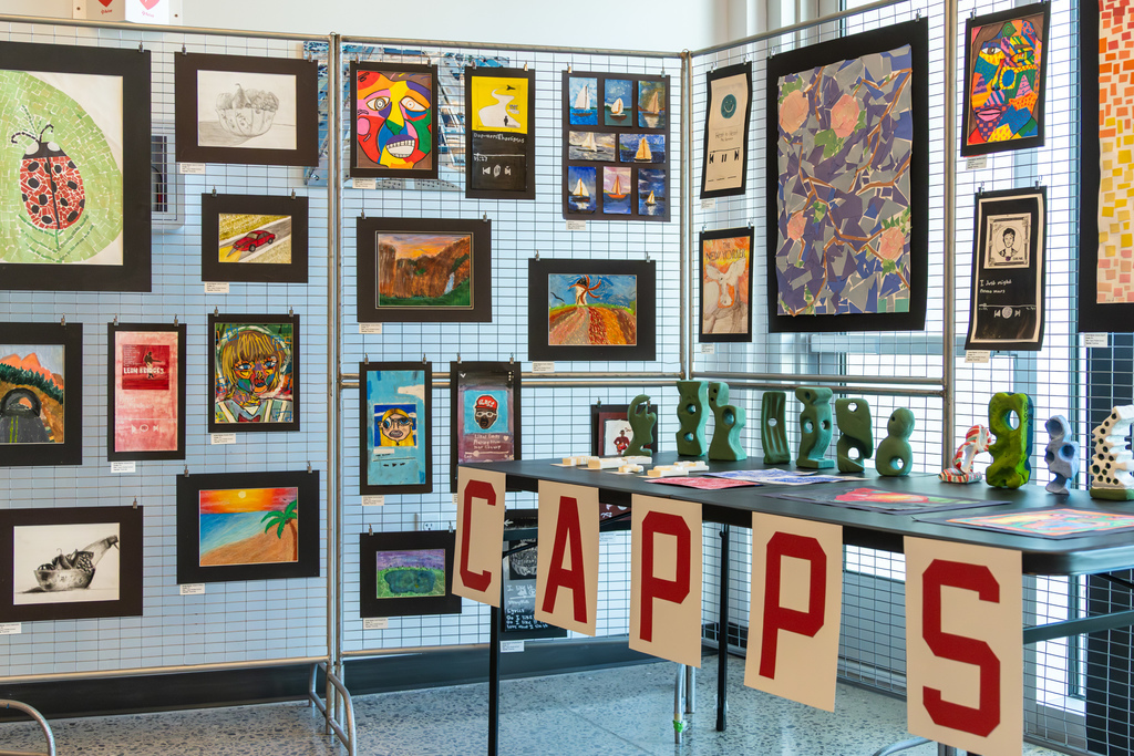 Student artwork hangs on display panels inside the Centennial Center during the Putnam City Arts Festival, with sculptures and a Putnam City Schools display table in front.