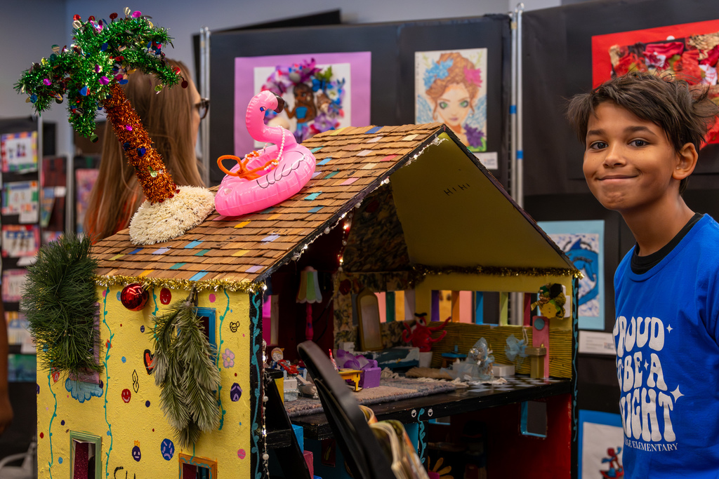 A student stands beside a colorful miniature house art project on display at the Putnam City Arts Festival.