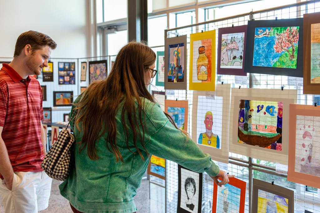 Two visitors look closely at student artwork displayed on panels inside the Centennial Center.