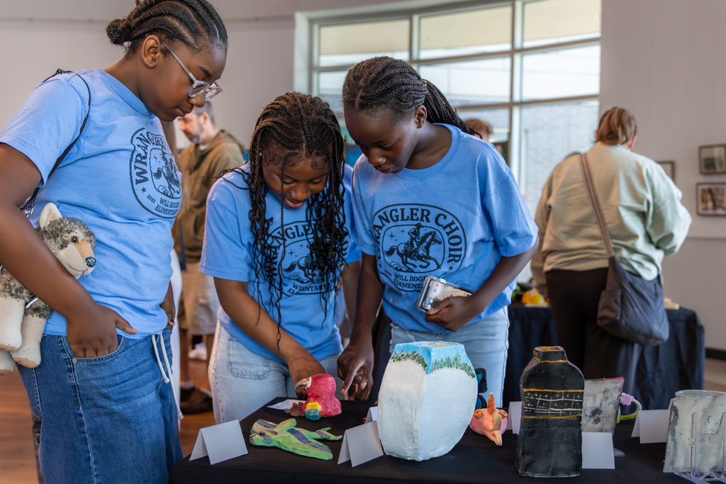 Three Will Rogers Elementary choir students look closely at ceramic pieces on display during the Putnam City Arts Festival.