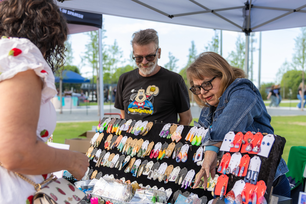 Visitors browse handmade earrings at an outdoor vendor booth during the Putnam City Arts Festival.