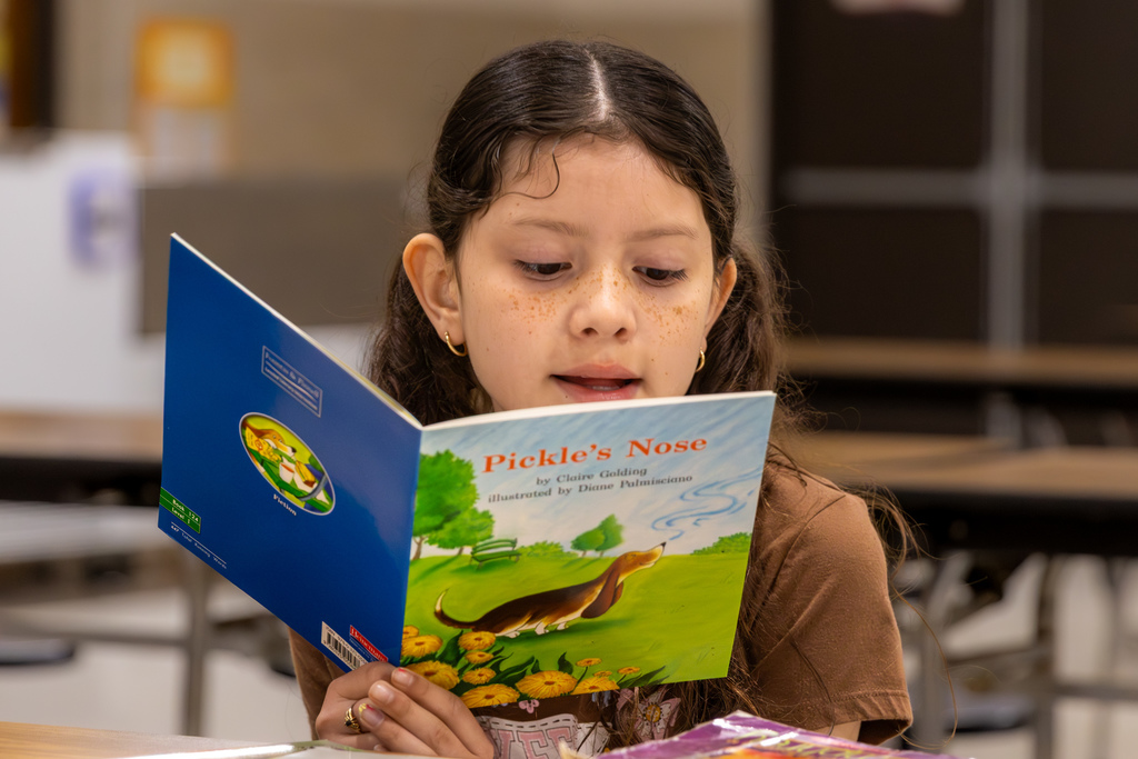 A student reads a copy of Pickle’s Nose while seated at a cafeteria table during Overholser Elementary’s Free Book Fair.