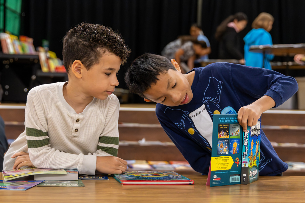 Two students look through books together at a cafeteria table during Overholser Elementary’s Free Book Fair.
