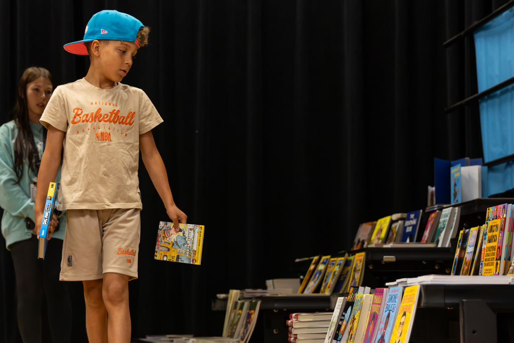 A student walks along the cafeteria stage while looking at books displayed for Overholser Elementary’s Free Book Fair.