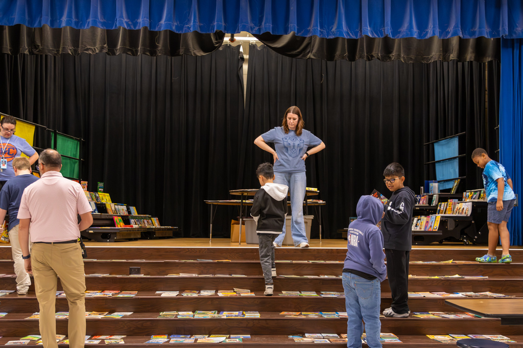 Students browse books arranged across the cafeteria stage while staff help during Overholser Elementary’s Free Book Fair.