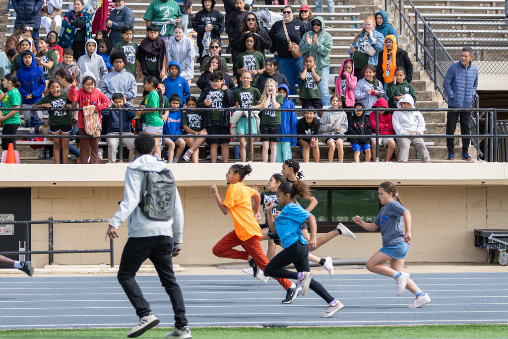 Students and families cheer from the bleachers as elementary runners race on the track below.
