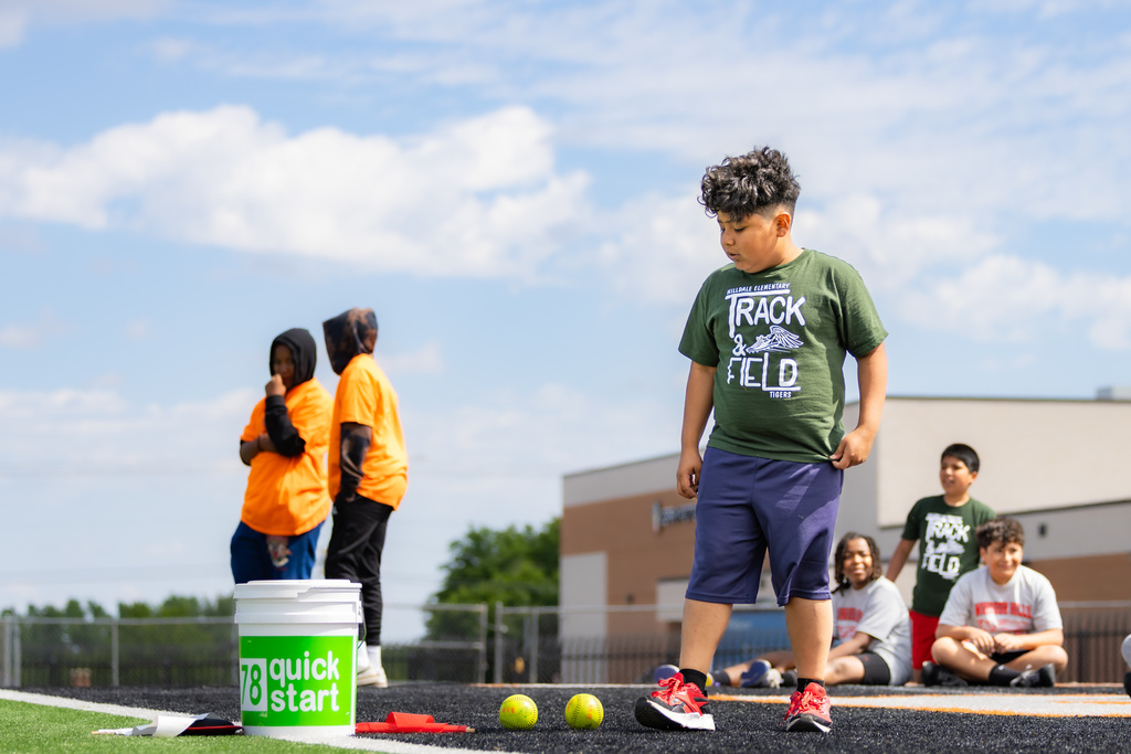 A Hilldale Elementary student stands near softballs and event equipment during the elementary track meet.