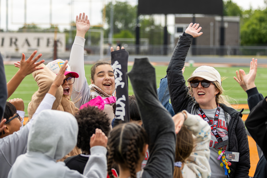Students and staff raise their hands together in a cheer during the elementary track meet.