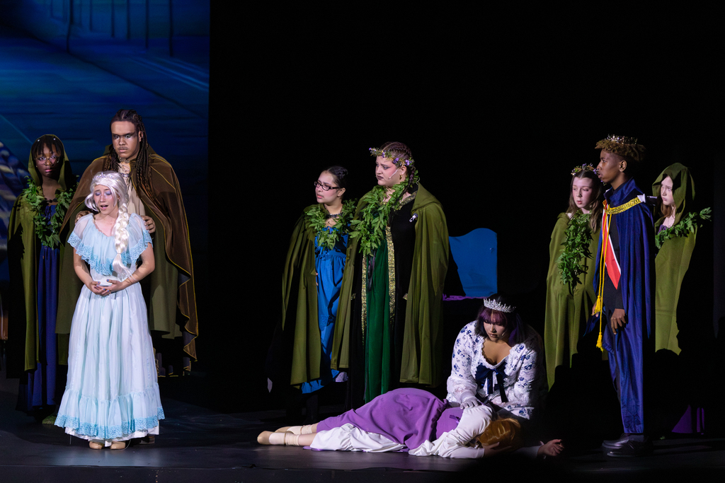 Putnam City North students perform a dramatic scene from Frozen: The Broadway Musical, with Elsa standing to the side as other cast members gather around Anna on stage.
