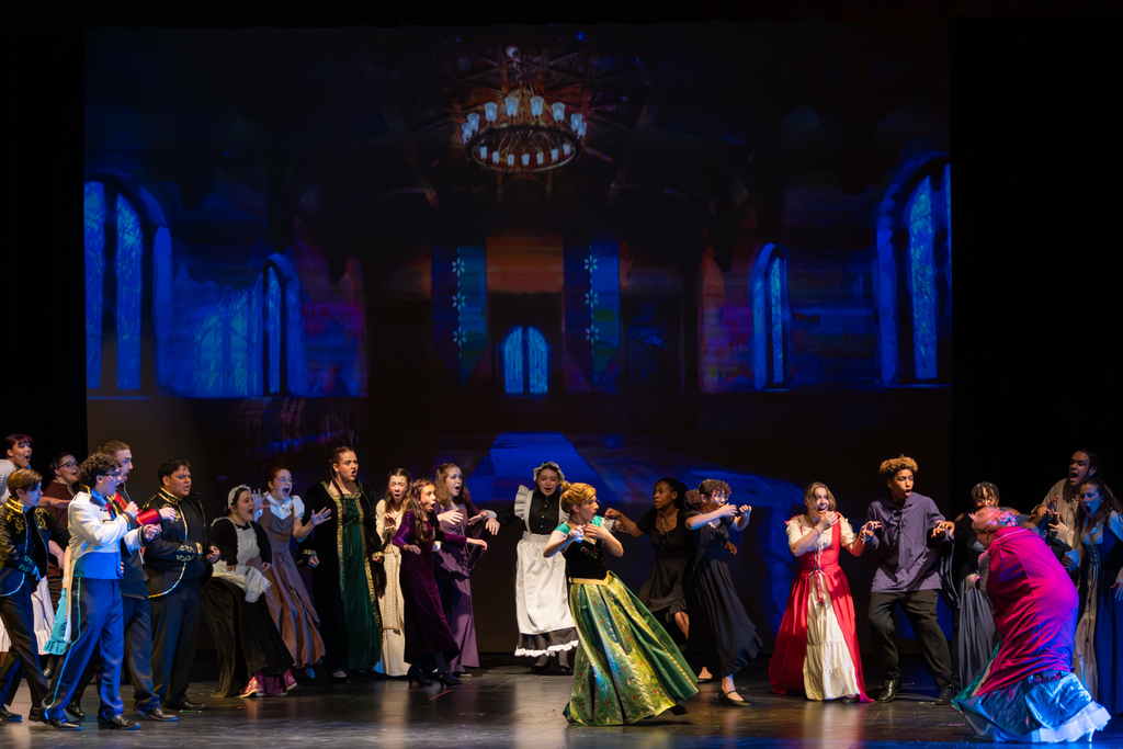 Putnam City North students perform an ensemble scene from Frozen: The Broadway Musical, reacting together on stage in front of a large projected castle backdrop.