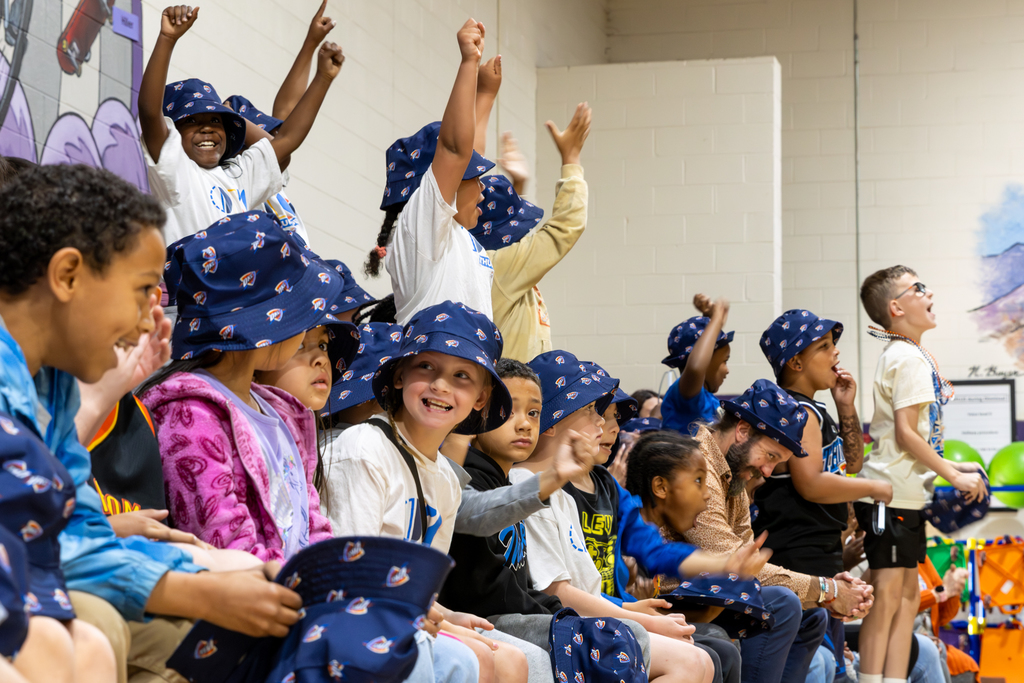 Rollingwood Elementary students cheer from the bleachers while wearing Oklahoma City Thunder hats during a schoolwide celebration.