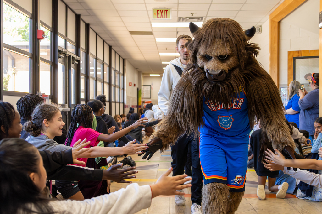 Rumble walks through a hallway of cheering Rollingwood Elementary students giving high-fives during the Thunder Reading Challenge celebration.
