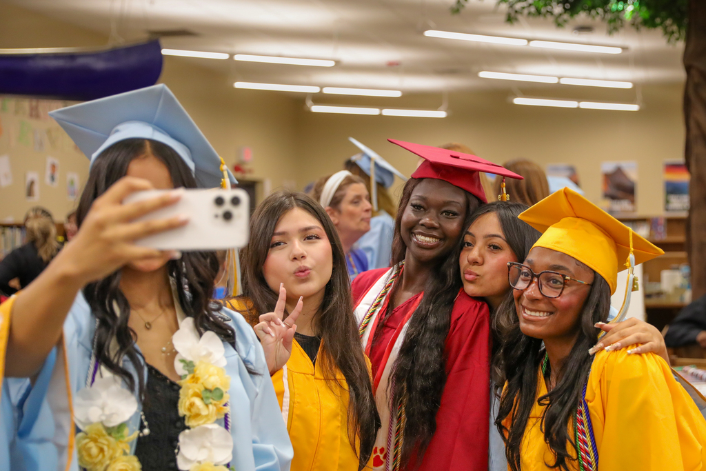 Putnam City seniors in red, gold and light blue caps and gowns gather for a selfie during a Grad Walk visit.
