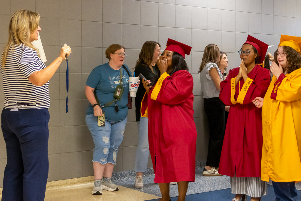 Putnam City seniors in red and gold caps and gowns react as staff members greet them during a Grad Walk at an elementary school.