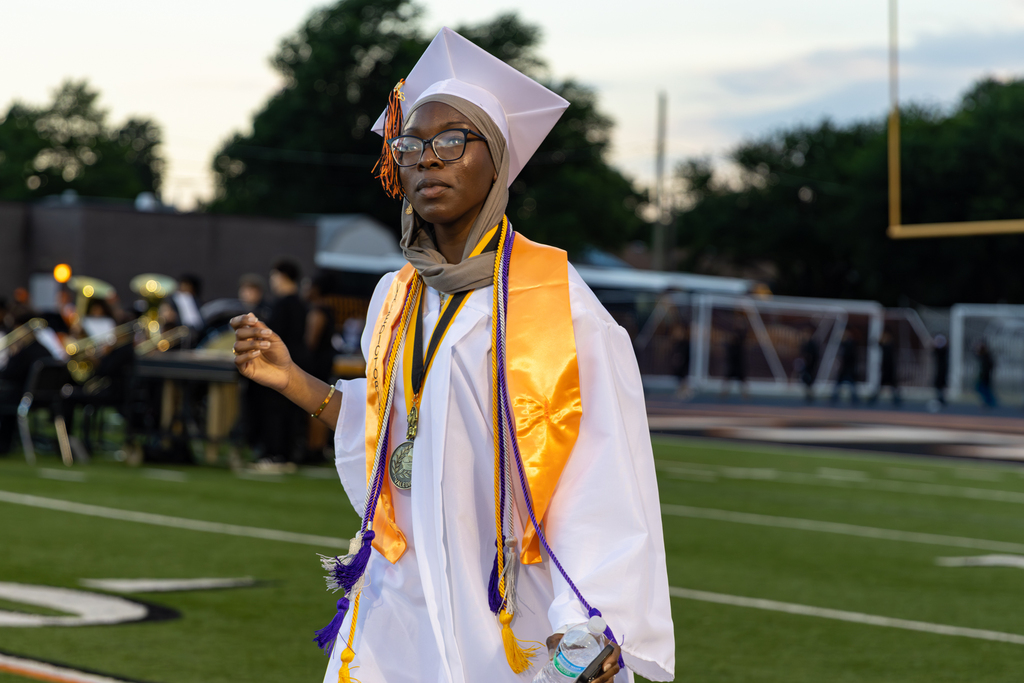 Student in white graduation gown with multiple cords and regalia