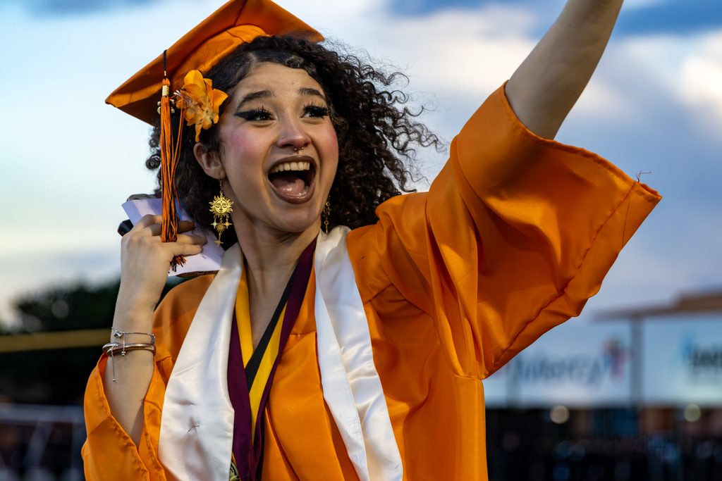 Smiling and waving student in a gold graduation gown