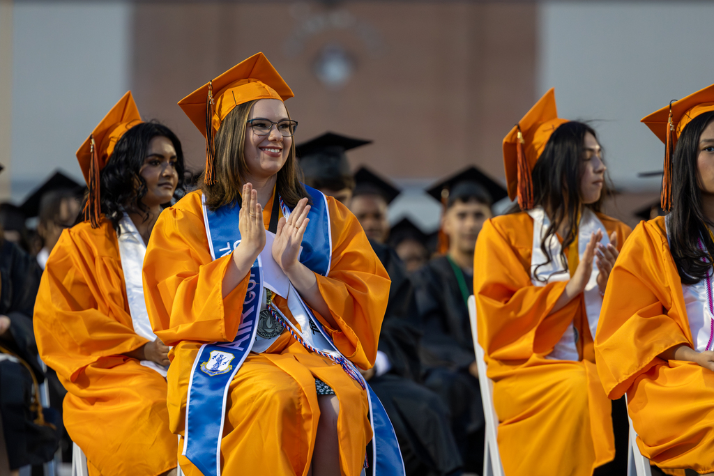 Clapping students wearing gold graduation gowns