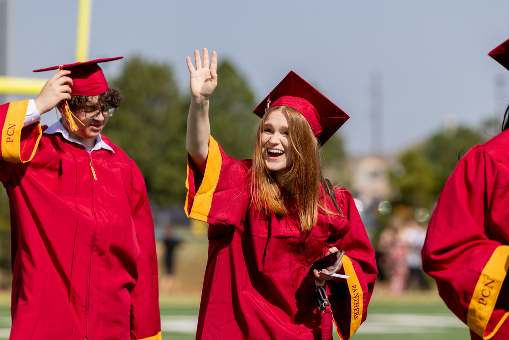 A Putnam City North graduate in a red cap and gown smiles and waves during the graduation ceremony.